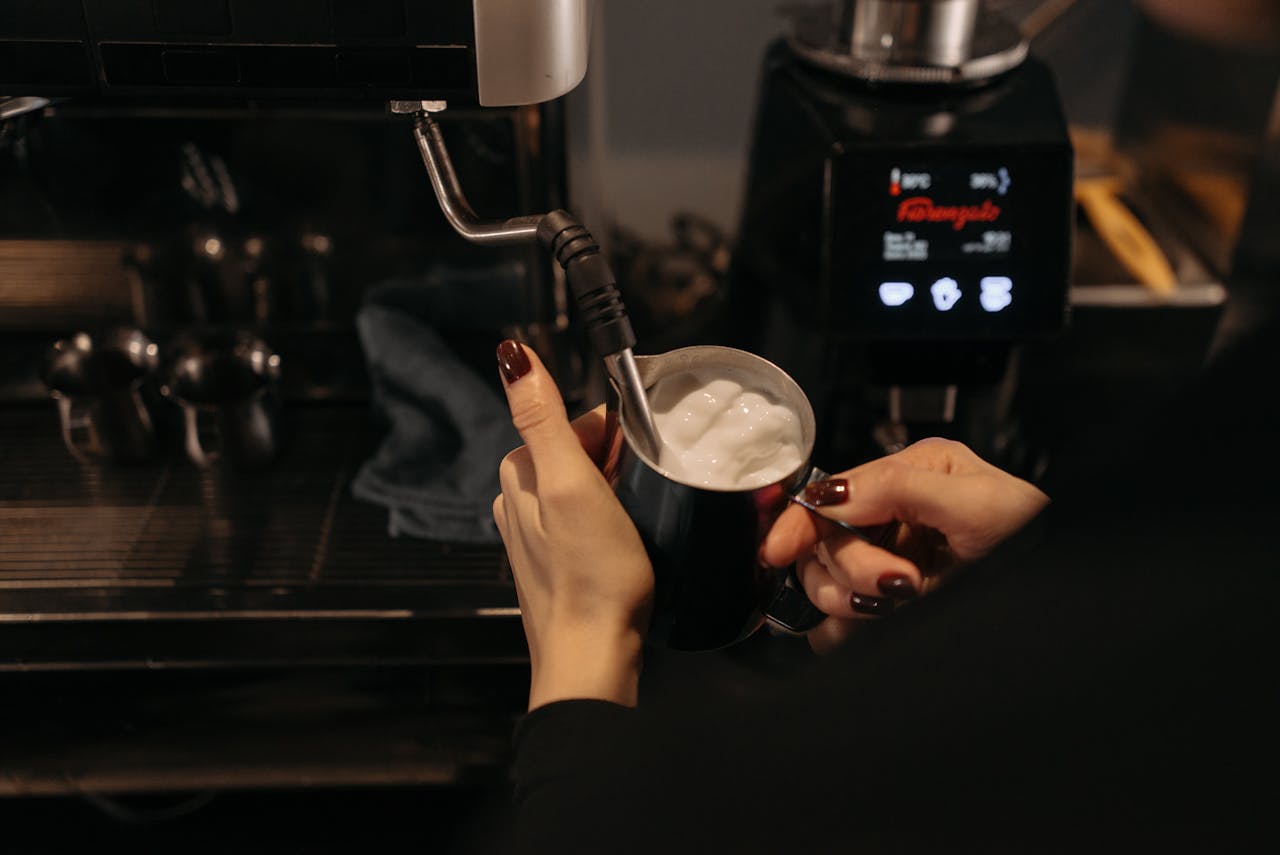 about-03 A barista uses a steam wand to froth milk in a café, focusing on coffee preparation.